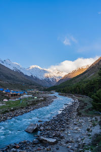 Scenic view of stream by mountains against blue sky