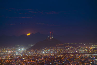 High angle view of moon rising over cityscape at night
