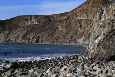 Scenic view of rocks and mountains by seascape against blue sky