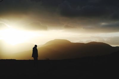 Silhouette man photographing mountains against sky during sunset