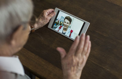 Senior man using mini tablet for skyping with his grandson