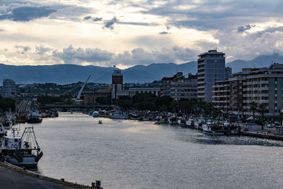 Sailboats moored on harbor by buildings in city against sky