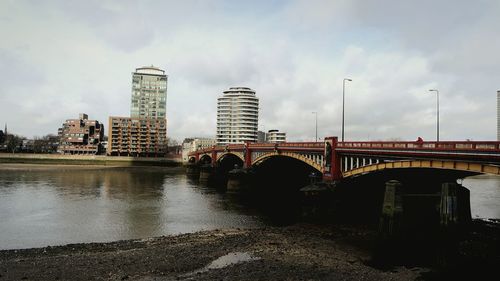 Bridge over river by buildings against sky in city