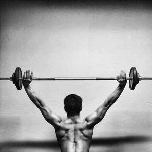 Rear view of shirtless muscular man exercising with barbell by wall