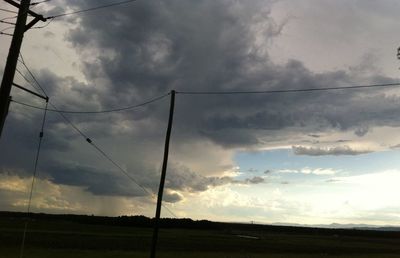 Electricity pylon on field against cloudy sky