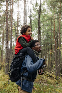 Side view of father carrying son on shoulder while exploring forest during vacation