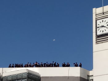 People on building against clear blue sky