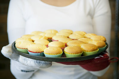 Midsection of woman holding muffins in tray