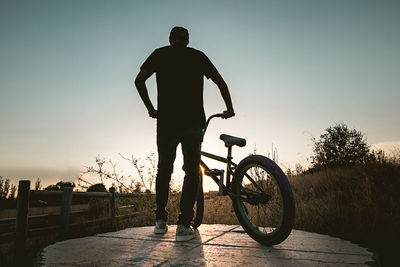 Rear view of man standing by bicycle against sky