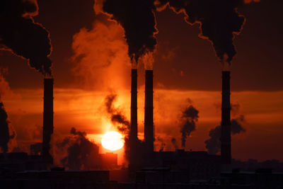 Coal-fired power station with smoking chimneys against red sunset sky. air pollution in winter city