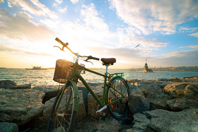 Bicycle on beach against sky during sunset