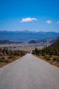 Empty road leading towards mountains against blue sky