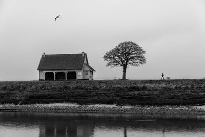 House on field by lake against clear sky