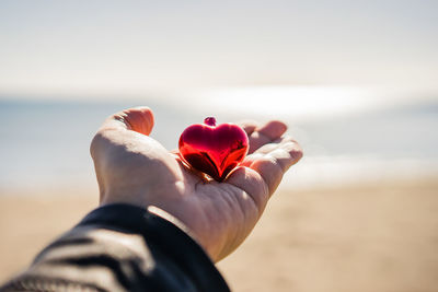 Close-up of hand holding red rose in sea