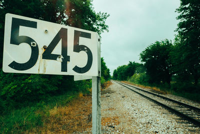Road sign by railroad tracks against sky