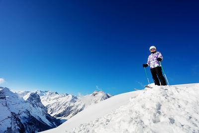 Rear view of man skiing on snowcapped mountain against clear blue sky