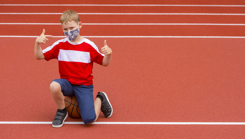 Full length portrait of boy sitting against red wall