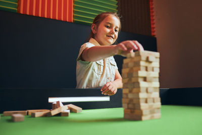 Little girl playing jenga game in play room. child building tower with wooden blocks. play and fun