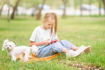 Full length of girl using phone with dog outdoors