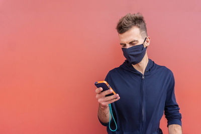 Young man using mobile phone against orange background