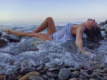 Young woman on rocks at beach against sky