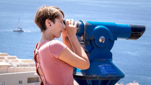 Side view of young woman looking through coin-operated binoculars at beach