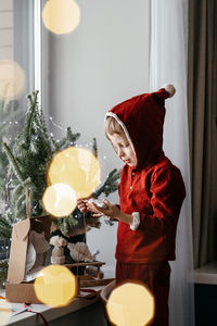 A thoughtful boy in a santa costume sits at the window and unpacking gifts