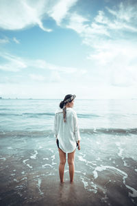Woman standing at beach against cloudy sky