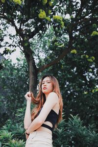 Young woman standing by tree against plants