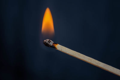 A close-up of a single match lit in front of a dark background. 