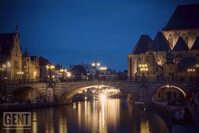 Illuminated bridge over river by buildings against sky at night