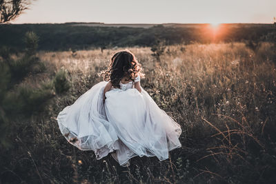 Rear view of woman standing on field against sky during sunset