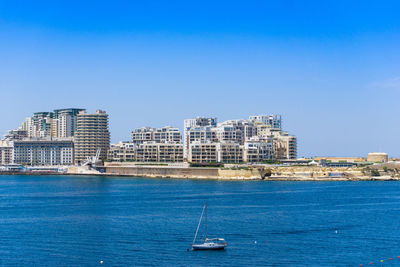 Boat on sea by buildings against clear blue sky in city