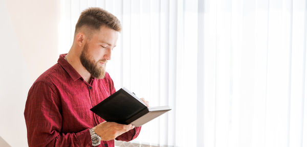 Business bearded man stands against window in office and writes down plans