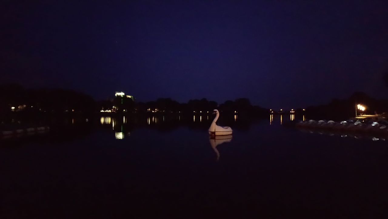 ILLUMINATED CITY BUILDINGS BY LAKE AGAINST SKY AT NIGHT