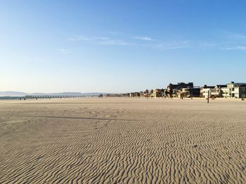 Beach by city against sky during sunny day