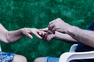 Old man painting his wife's nails red sitting on a chair