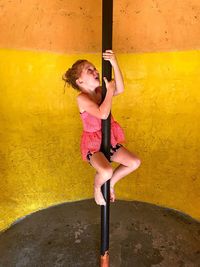 Girl climbing on pole against yellow wall