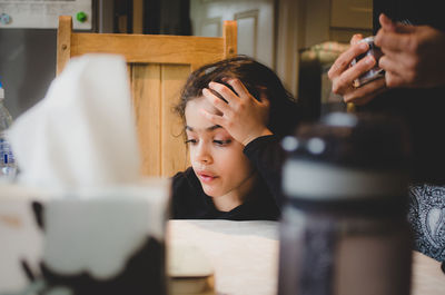 Contemplating girl sitting by table at home