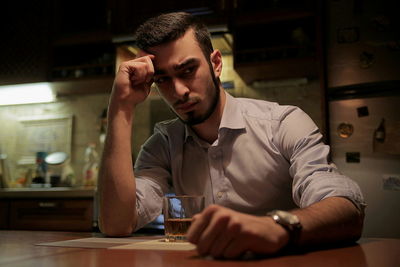Sad businessman drinking whiskey while sitting at table in kitchen