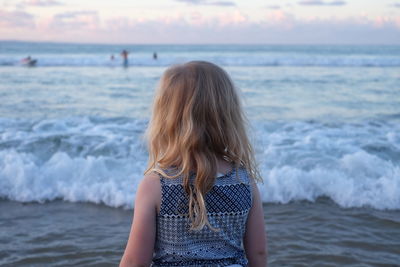 Rear view of girl standing on beach against sky