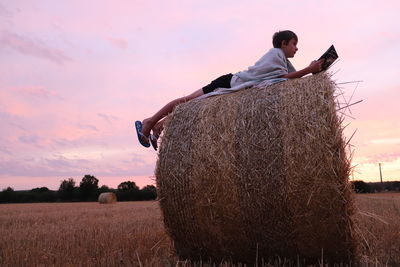 Boy using digital tablet on hay against sky during sunset