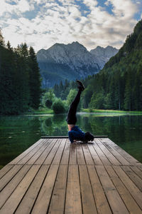 Man practicing yoga on lake against mountain