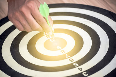 Cropped hand of man holding dart on board