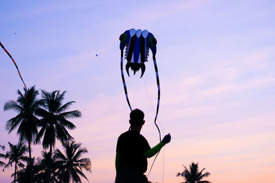Silhouette man flying kite against sky at sunset
