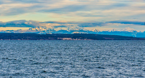 Scenic view of sea by snowcapped mountains against sky