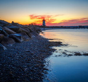 Lighthouse by sea against sky during sunset