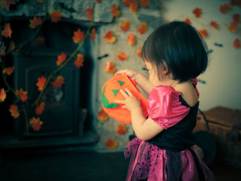 Close-up of baby girl holding jack o lantern basket at home