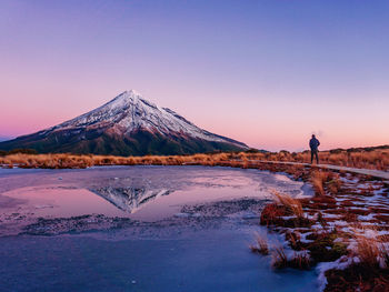 Person standing on shore against sky during sunset