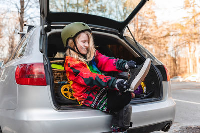 Delighted girl in protective helmet taking off sneakers and preparing for rollerblading in autumn park